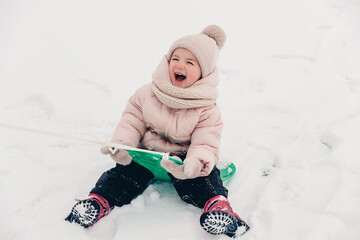 Happy laughing girl wearing a pink jacket, scarf and hat, playing in a beautiful snowy winter walk. Girl enjoys winter, frosty day. Playing with snow on winter holidays. Winter holidays concept.