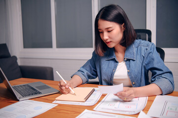 Professional Asian woman designer designing UI UX graphical user interface webs design sketching drawing on note book planning concept ideas on documents, working laptop home office working late night
