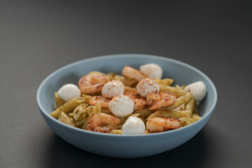 Penne pasta with shrimps and mozzarella and pesto in blue bowl
