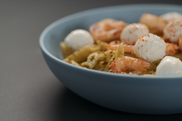 Penne pasta with shrimps and mozzarella and pesto in blue bowl with copy space