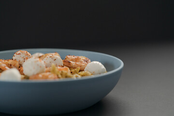 Penne pasta with shrimps and mozzarella and pesto in blue bowl with copy space