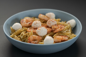 Penne pasta with shrimps and mozzarella and pesto in blue bowl