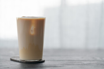 Ice coffee wih milk in tumbler glass on black oak table