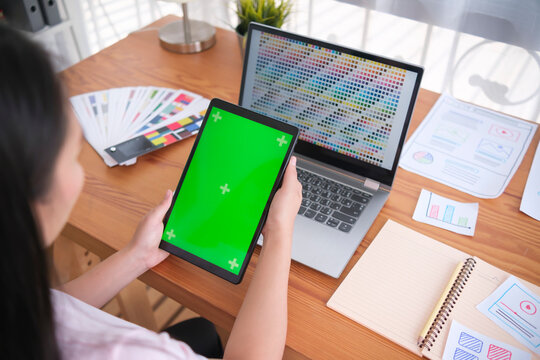 Mock up blank green screen tablet Young Asian woman freelance graphical designer UI UX designer web design concept ideas using computer technology software working home office workstation desk