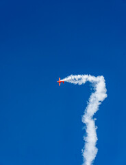 the red plane makes difficult turns and blows white smoke against the blue sky at the Max-21...