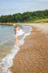 Fototapeta na wymiar woman in straw hat and swimsuit high-rise panties walk on beach by the sea and enjoying summer against summer hills. Fashionable swimming bikini with high fit. Summer sea vacation. selective focus