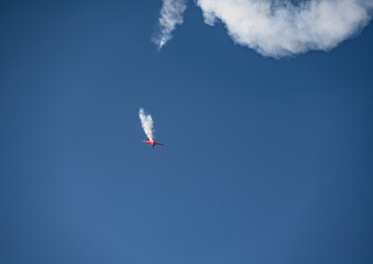 Fototapeta na wymiar the red plane makes difficult turns and blows white smoke against the blue sky at the Max-21 aerospace salon in Zhukovsky on July 24, 2021