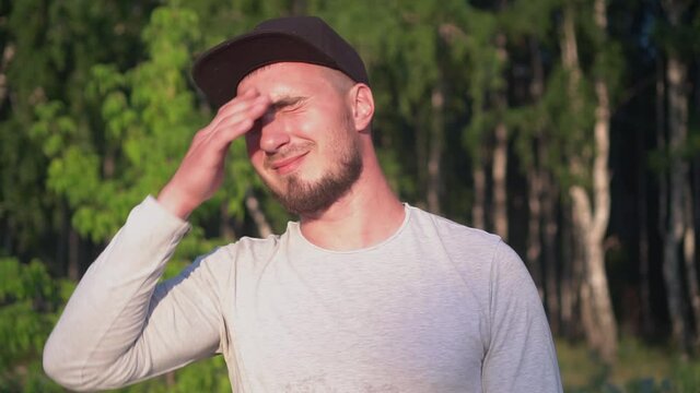 A Man in a Baseball Cap Who Blinds the Bright Sun, Closes His Eyes and Covers His Face
