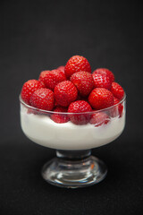 strawberries in a glass bowl with whipped cream on a dark grey background