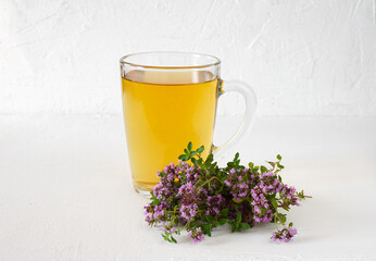 healthy tea with wild thyme in a glass mug on a white wooden background with flowers near