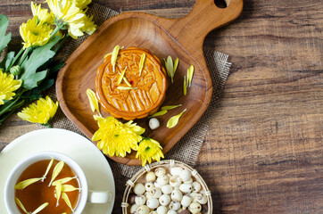 Top view of delicious homemade moon cake on wooden plate with flower tea and dry organic lotus seed on grunge background for Mid Autumn Festival in China concept