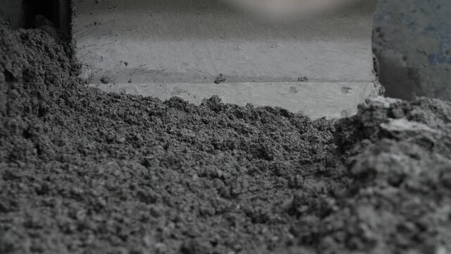 Close-up view of asphalt or concrete material mass moved by paver, spreader or road paving machine. Concept of roadwork operation with substance for roadbed construction, highway paving process.