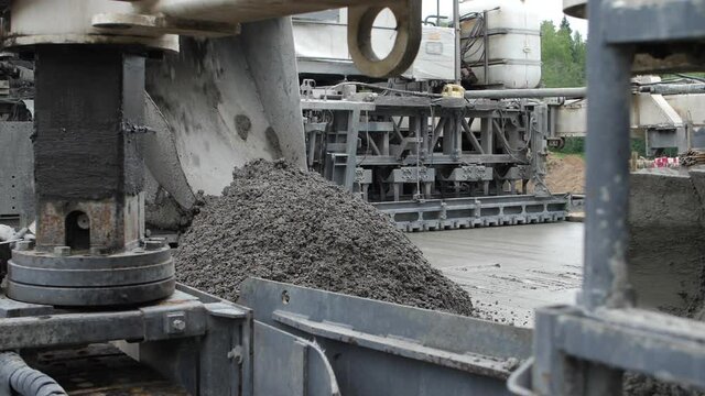 Road paving machine or slipform paver finisher dumping asphalt concrete mass on roadway surface to make screed. Concept of heavy-duty motorized vehicle for highway engineering and construction works.
