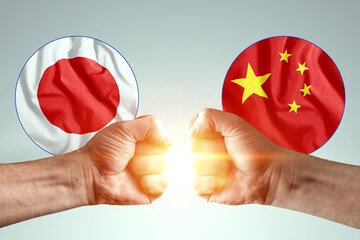 Male hands show their fists against the background of the flags of Japan and China. The concept of...