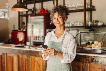 Fototapeta na wymiar Female cafe owner holding a smartphone in her shop