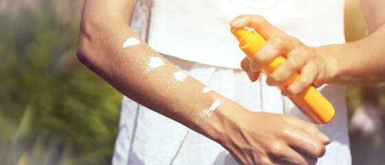 A young girl in a white dress applies sunscreen gel to her arms and shoulders.
