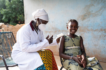 Courageous little African girl smiling into the camera while receivng a vaccine shot by a gentle...