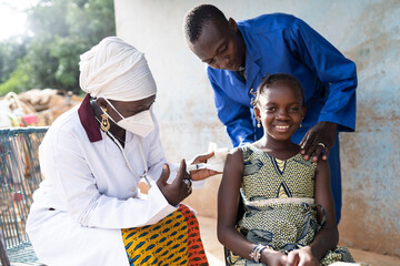 Beautiful brave little African girl with a big confident smile being vaccinated by a female doctor,...