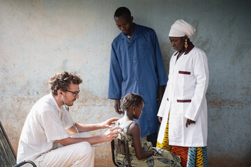 Two African physicians observing a young white doctor during auscultation of a small black girl's...