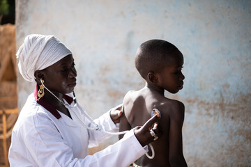 Attentive black African doctor examinating the respiratory and heart function of a small toddler...