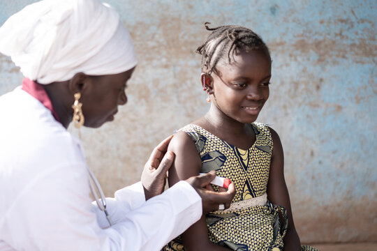 Closeup of a smiling little African girl undergoing axillary temperture measurement by a gentle black nurse