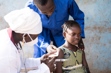 Relieved little African girl looked after by the vaccination staff after she has received her first...