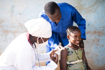 Smiling cute African girl being injected a vaccine dose in her upper arm by a black female...