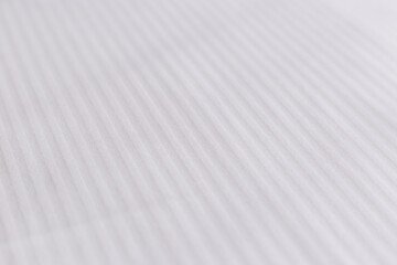 Elegant textile on bed. Striped pattern on a snow-white bedsheet.
