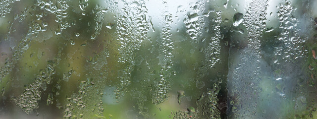 Rain drops on glass window. Raindrops falling from glass material. Abstract nature background. Copy space for text. Focus on foreground.