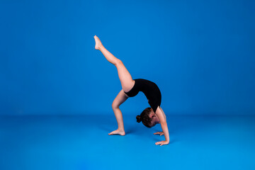 Fototapeta na wymiar a small gymnast in a black swimsuit stands on her hands on a blue background with a place for text