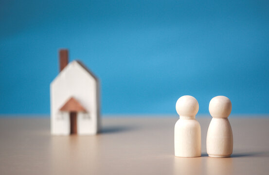 Two wooden figures of people with happiness and a house on blue background. Affordable housing and mortgages for buying concept young family and couples. family nest and copy space.