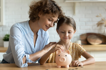 Little girl with mother putting coin into pink piggy bank, planning budget managing finances,...