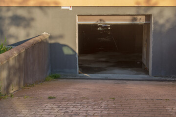 Open entrance to parking lot in basement of residential apartment building. Slope floor made of pink paving slabs, further of concrete screed, inside can see puddles. Shot was taken early in morning
