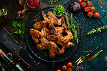 Grilled chicken wings with sauce and spices on a black stone plate. Top view. Free space for text.