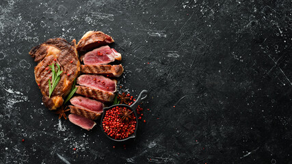 Grilled sliced beef steak with rosemary and spices on a black stone background. Top view. Free space for your text.