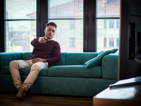 Handsome young man on counch, using TV remote control
