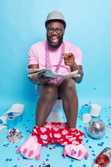 Funny positive dark skinned adult man wears spectacles hardhat t shirt points at camera and laughs...