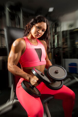 portrait of strong young female hispanic athlete with dumbbells at gym