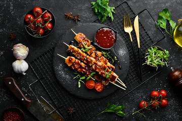Chicken skewers with teriyaki sauce on a black stone plate. Rustic style. Barbecue menu.