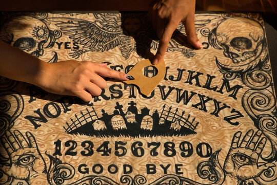Detail of young hispanic and latin women's hands on a ouija board pointing to the letter h.