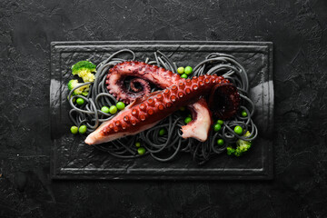 Black pasta with octopus tentacles on a black stone plate. Seafood. Top view. Free space for your text. © Yaruniv-Studio