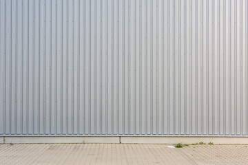 Exterior wall of warehouse made of aluminum sheet and paved road in outdoor area as background image. Texture of a wall made of silver corrugated metal sheets