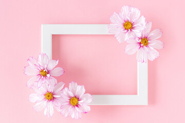 White wooden frame decorated with flowers on a pink background. Flat Lay Top view Copy space
