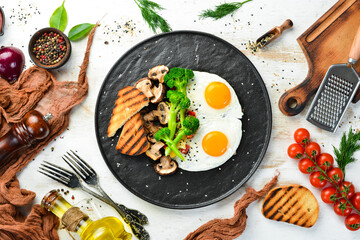 Healthy breakfast. Fried egg with broccoli, mushrooms and bread. On a black stone plate. Top view.