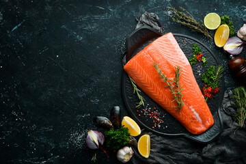 Raw salmon fillet with rosemary on a black stone plate. On a dark background. Flat lay. - obrazy, fototapety, plakaty