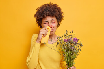 Photo of frustrated Afro American woman suffers from allergic rhinitis rubs nose with napkin holds...