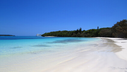 Turquoise water white sandy beach with a cruise ship docking on the background in Isle of Pines, New Caledonia.