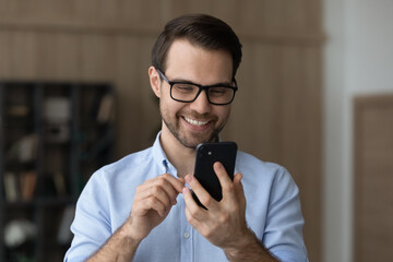 Perfect mood. Smiling young adult guy wear glasses hold mobile telephone read good message received...