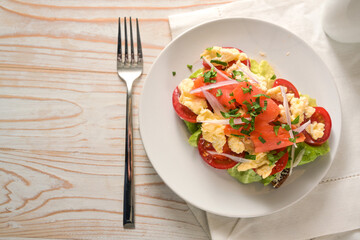 Sandwich with tomatoes, scrambled eggs and smoked salmon on a white plate and a bright wooden table with copy space, high angle view from above