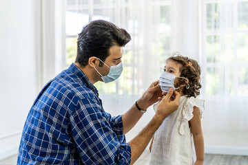 Father is wearing the face mask for little daughter, both are wearing face masks for confidence in their health. Protect themselves from dangerous spread of coronavirus covid-19